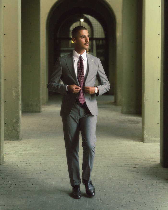 gallery-1 Man in gray suit and tie walking confidently through an archway, embodying modern elegance.