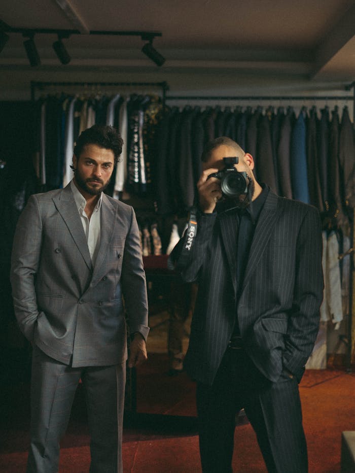 Pourquoi choisir Santorio Two men in suits, one taking a photo, in a fashion boutique setting.